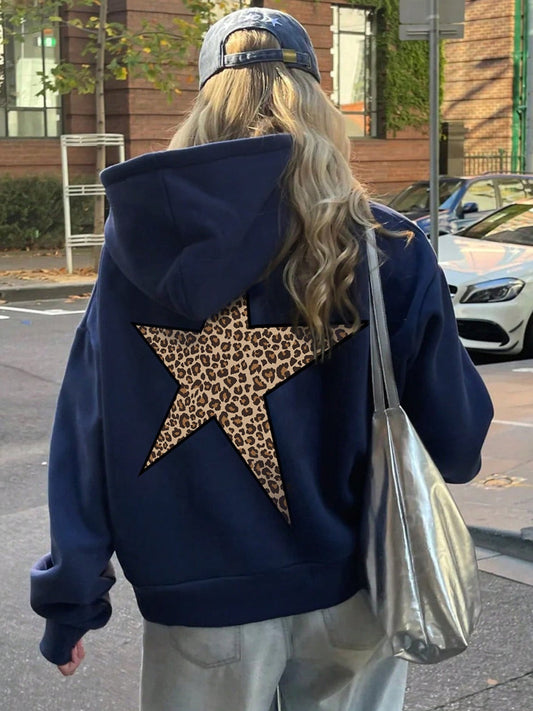 Person wearing a blue hoodie with a leopard print star on the back, standing on a street.